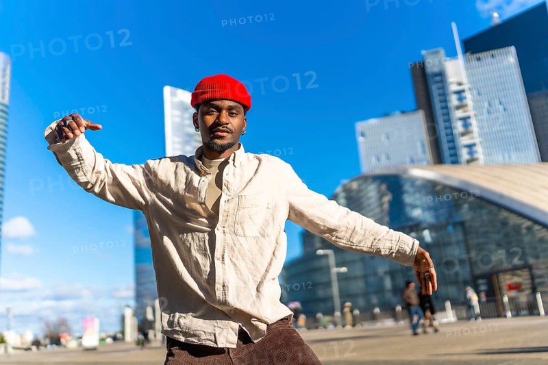 Young black man showing movement and expressing himself through dance in an urban setting with modern skyscrapers and architecture under a clear blue sky