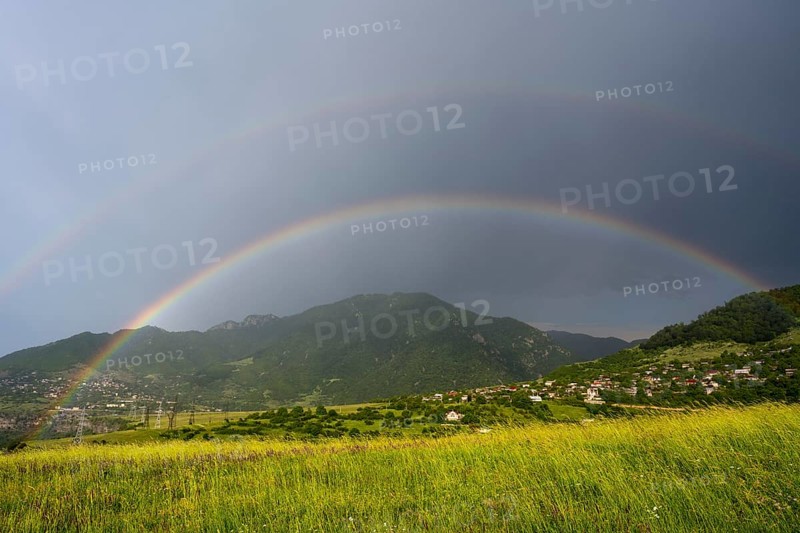 Two rainbows stretch across a green landscape with mountains and a village under a cloudy sky, Lorikeet province, Armenia