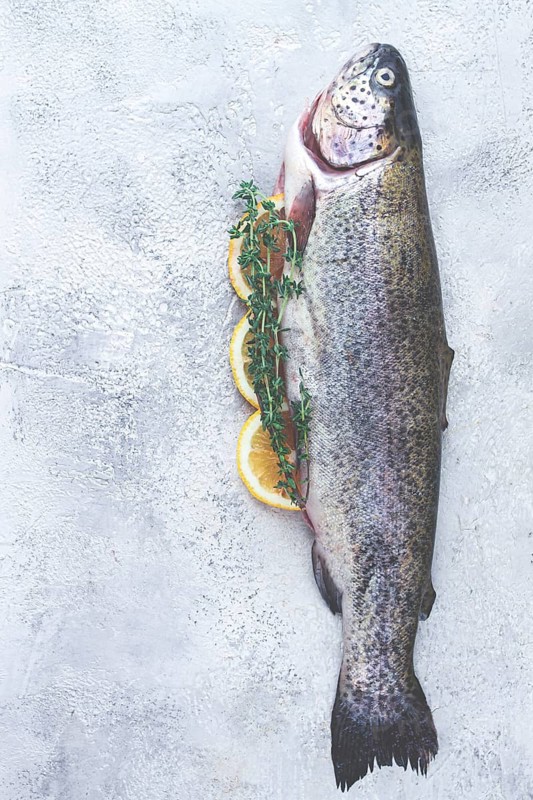 Freshly caught rainbow trout with herbs and citrus arranged on a light textured surface