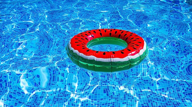 A bright ring-a float, with a watermelon, in the clear blue water of the pool, under the sunlight