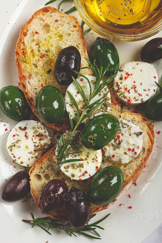 A plate with a snack, ciabatta bread with cheese and olives, olive oil, spices and herbs, top view, no people