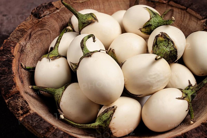 White mini eggplant, in a wooden bowl, on the table, close-up