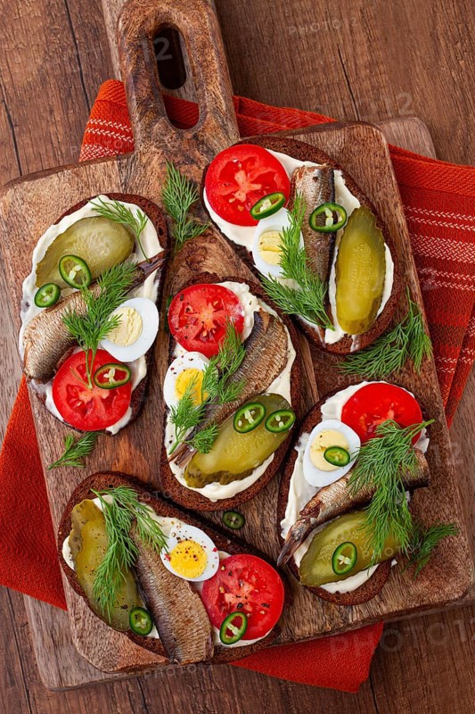 Sandwiches on rye bread with sprats, quail eggs, fresh tomatoes and pickled cucumber, on a wooden board, appetizer, breakfast
