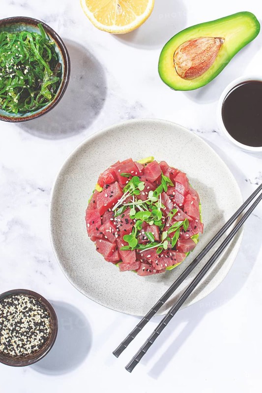 Fresh tuna tartare with avocado served on a marble table with soy sauce and seaweed salad