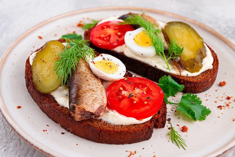 Sandwiches on rye bread, with sprats, quail eggs, fresh tomatoes and pickled cucumber, appetizer, breakfast, homemade