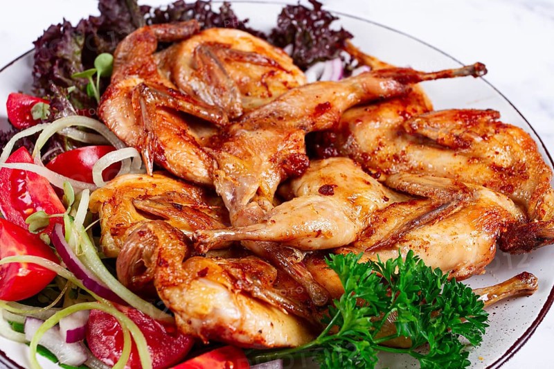 Baked quail, served on a plate with crispy lettuce leaves, fresh tomatoes and herbs, on a white plate, homemade
