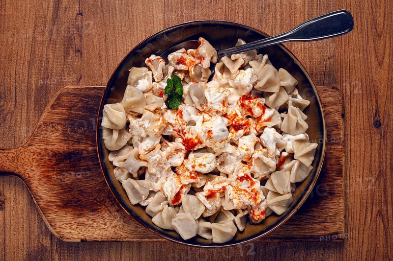 The dish features a generous serving of Turkish dumplings topped with velvety yogurt and a drizzle of spicy red sauce