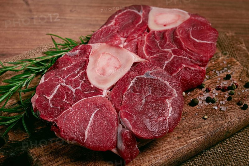 Knuckle on the bone, raw meat for ossobuco, on a wooden chopping board, with a sprig of rosemary, and spices, top view, no people