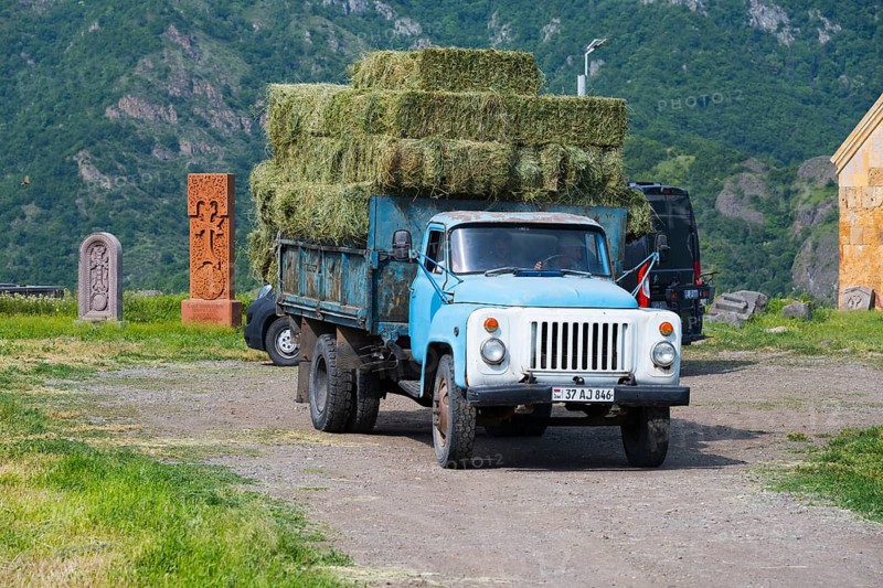 A blue truck with hay bales drives on a dirt road surrounded by mountains and fields, classic car, GAZ-53, near Odsun, Odzun, Lorikeet province, Armenia