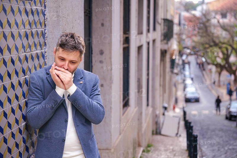 Man musician in a blue blazer and white sweater playing blues on a harmonica with eyes closed, standing outdoors in city street
