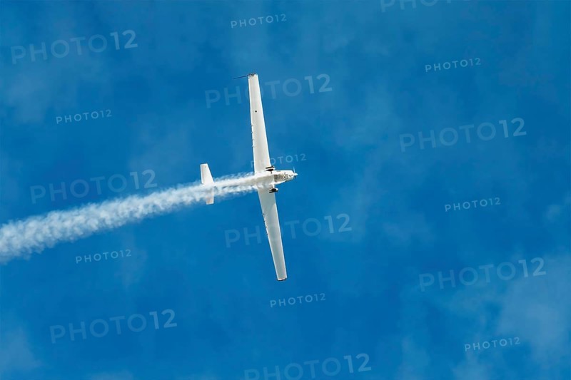 Stunt aerobatic plane performing stunts in blue sky with smoke trail. Concept of speed, difficulty, precision, risk, challenge