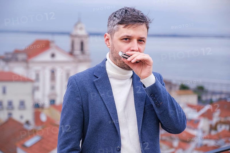 Man musician in a blue blazer and white sweater playing blues on a harmonica with eyes closed, standing outdoors in Lisbon city street, Portugal