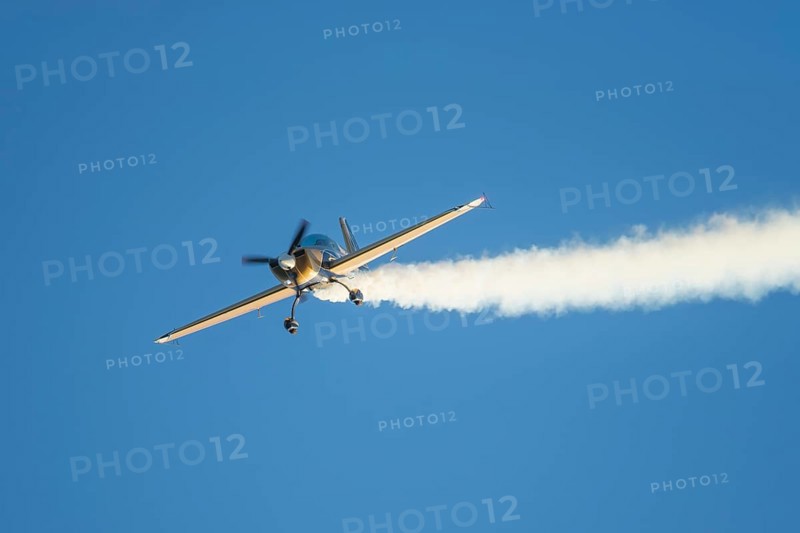 Golden stunt aerobatic plane performing stunts in blue sky with smoke trail. Concept of speed, difficulty, precision, risk
