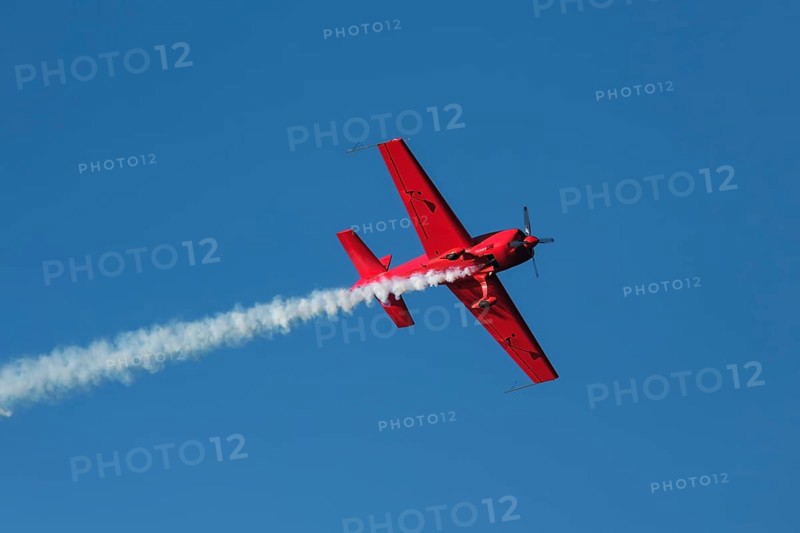 Red stunt aerobatic plane performing stunts in blue sky. Concept of speed, difficulty, precision, risk