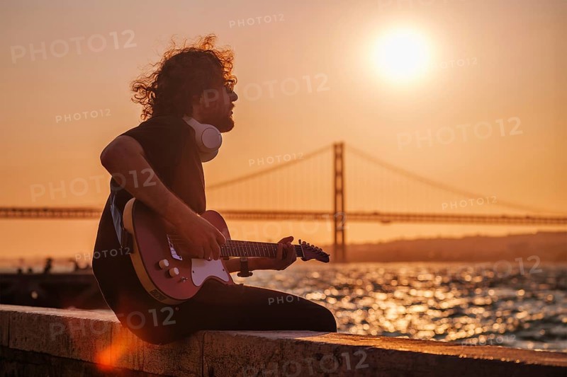 Hipster street musician in black playing electric guitar in the street on sunset