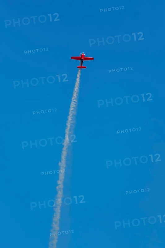 Red stunt aerobatic plane performing stunts in blue sky. Concept of speed, difficulty, precision, risk