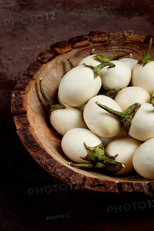 White mini eggplant, in a wooden bowl, on the table, close-up