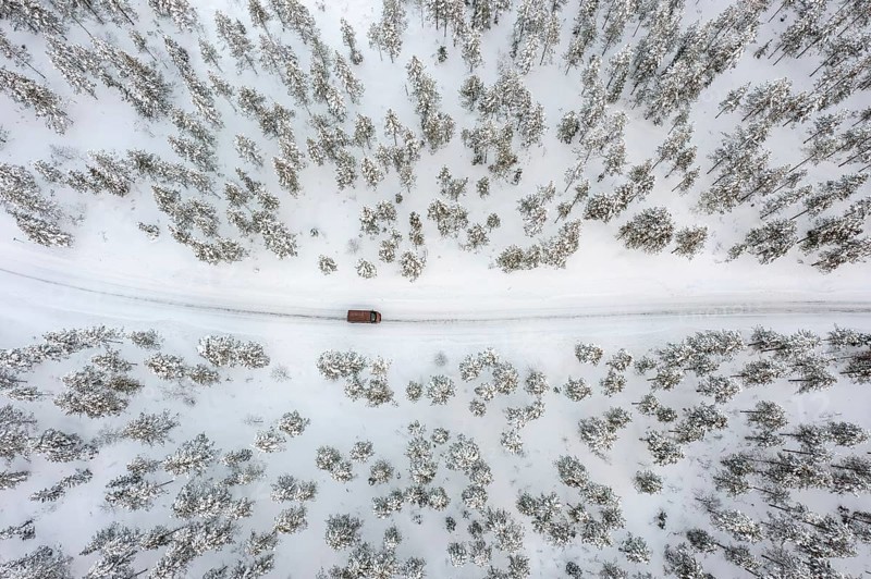 Aerial view over car, van driving over snow covered road through the taiga in winter, Riisitunturi National Park, Lapland, Posio, Koillismaa, Finland