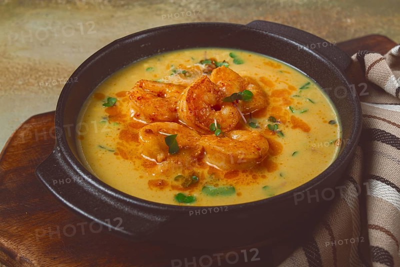 Creamy shrimp curry with spices, garnished with herbs, on a textured background, homemade, no people