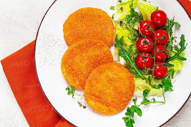Crispy fried fish cutlets, fish burgers, on a white plate, with fresh lettuce leaves, arugula and cherry tomatoes, homemade, no people