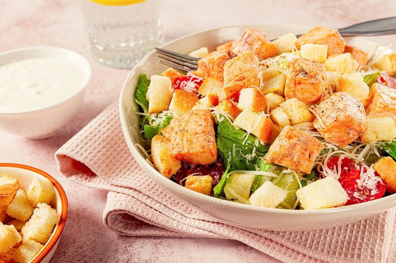 Caesar salad with salmon, with croutons and dressing, in a salad bowl, on a pink table