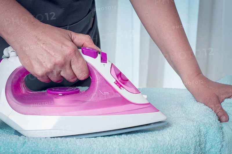 Ironing clothes at home, in a bright room, with natural light, female hands