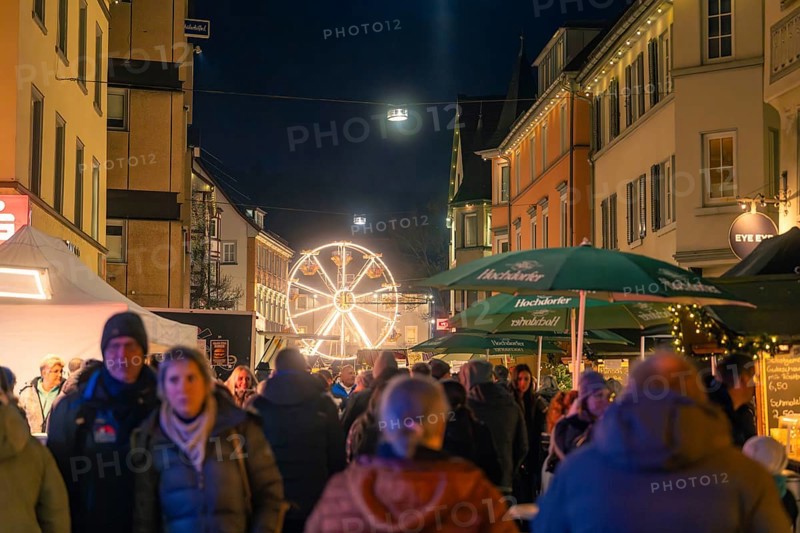 A Ferris wheel in the distance illuminates a busy street of a Christmas market, Christmas market 2025, Nagold, Black Forest, Calw district, Germany