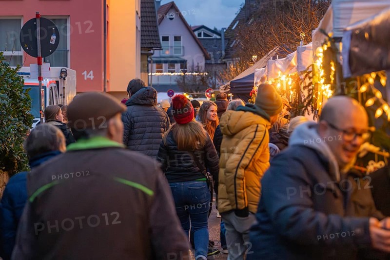 People stroll through an illuminated night market in a street, Aidlingen Christmas market, Böblingen district, Germany