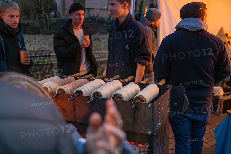Vendors at a stand at a Christmas market prepare traditional tree striezel under evening lighting, Aidlingen Christmas market, Böblingen district, Germany