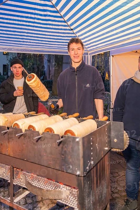 A market stand selling tree strips. A smiling person shows a tree striezel, Aidlingen Christmas market, Böblingen district, Germany