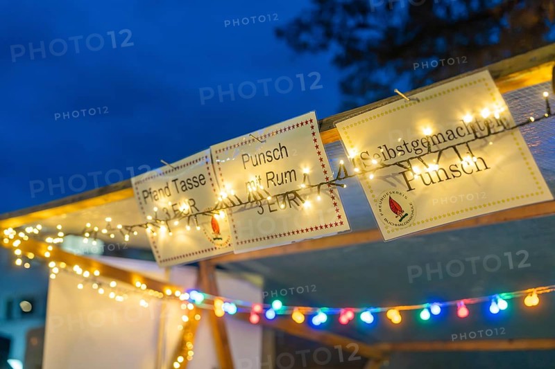Glowing signs and fairy lights draw attention to a punch stand in the evening, Aidlingen Christmas market, Böblingen district, Germany