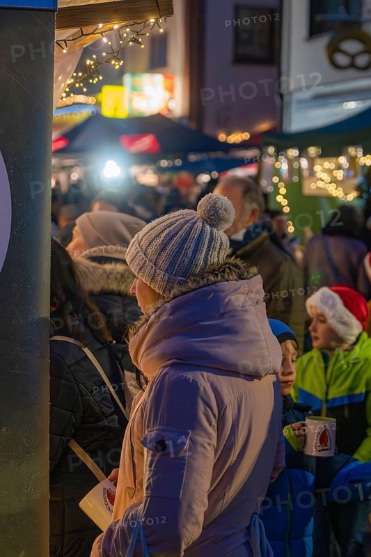 Woman in warm winter clothes holding coffee cup surrounded by children and twinkling lights at the market, Aidlingen Christmas market, Böblingen district, Germany