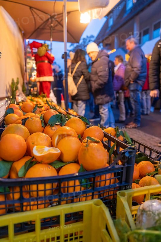 Fresh oranges in boxes in front of curious market visitors in the evening, Aidlingen Christmas market, Böblingen district, Germany