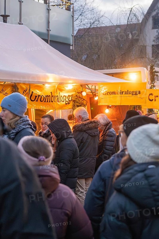 People stand at a brightly lit stand at a Christmas market, wrapped in warm clothes, Aidlingen Christmas market, Böblingen district, Germany