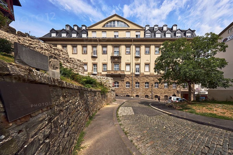 Sandstone wall, historic building, house, faÃ§ade with windows, dormers, asphalt sidewalk, cobblestone street, trees, meadow, blue sky, altocumulus clouds, cirrus clouds, street Am Römertor, Wiesbaden, state capital, district-free city, Hesse, Germany