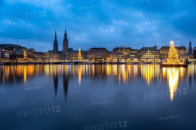 The decorated and illuminated Alster fir tree on the Inner Alster with reflections on the water in December at blue hour with the main church of St. Michaelis and town hall, Jungfernstieg, Hamburg, Germany