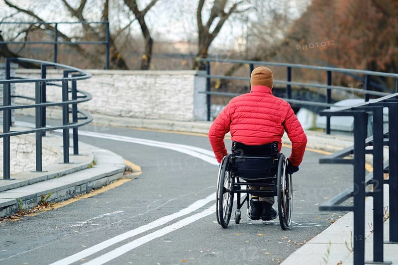 Active person in a red jacket uses a wheelchair to move along a winding path