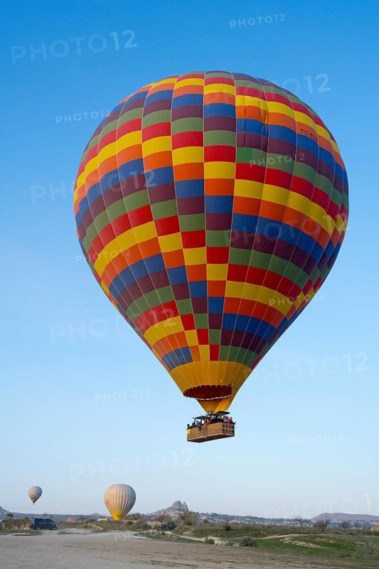 A colorful hot air balloon floats in daylight over a meadow under clear blue sky, Göreme National Park, Göreme Tarihî Millî Parki, Nevsehir Province, Nevsehir, Cappadocia, Cappadocia, Central Anatolia, Turkey