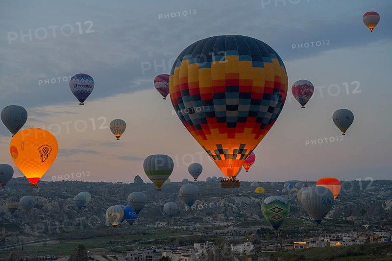 Colourfully patterned hot air balloons rise over the city and countryside of Cappadocia, Göreme National Park, Göreme Tarihî Millî Parki, Nevsehir Province, Nevsehir, Cappadocia, Cappadocia, Central Anatolia, Turkey