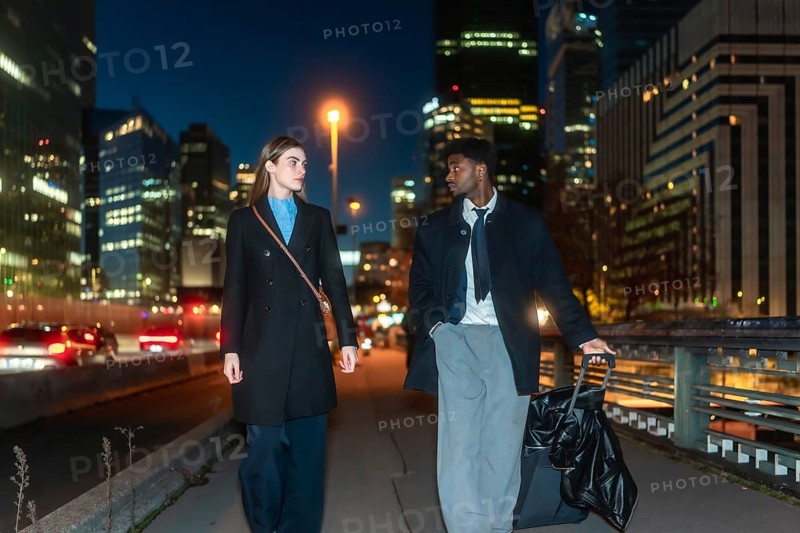 Business colleagues traveling together, walking on a city bridge with their luggage at night, showcasing urban lifestyle and dynamic career aspirations in a modern metropolitan area