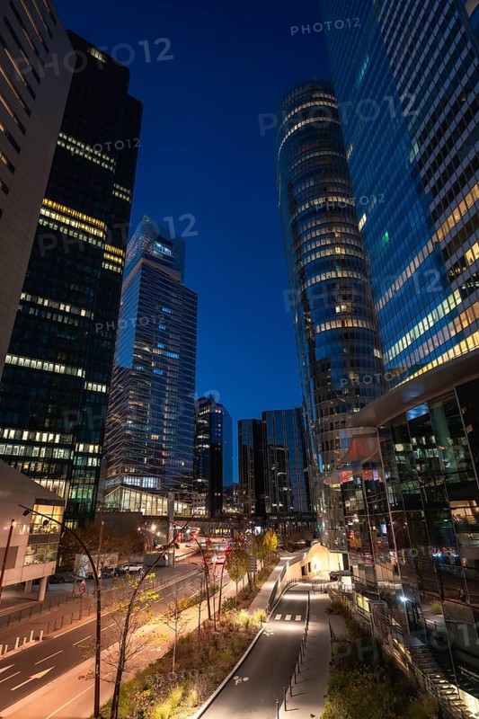 La defense financial district in paris at twilight, modern glass skyscrapers with illuminated offices reflecting blue hour light, conveying finance, business and urban growth