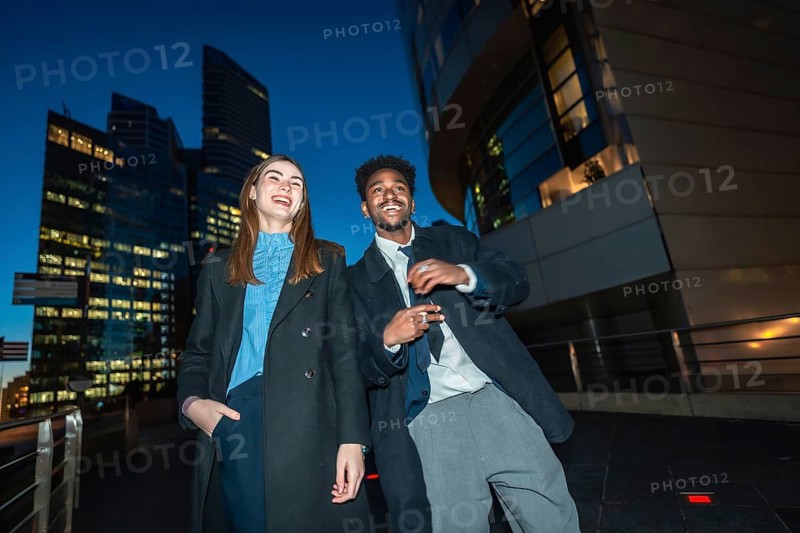 Diverse businesspeople enjoying a joyful moment together while standing on a promenade with illuminated city skyscrapers in the background during a vivid evening