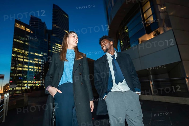 Diverse business professionals sharing a cheerful moment, smiling and talking under the city lights at night, representing successful communication and partnership in a modern urban environment