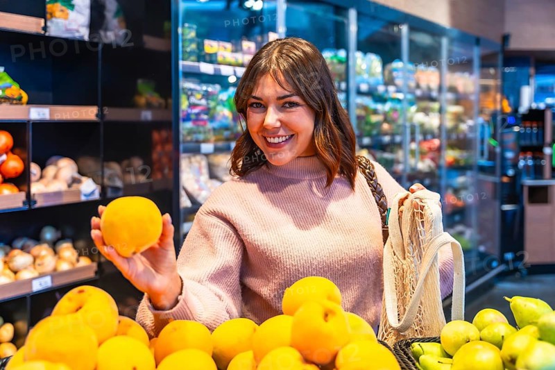 Young woman shopping for organic produce in a grocery store, holding a fresh yellow fruit and smiling, promoting healthy eating habits and sustainable choices