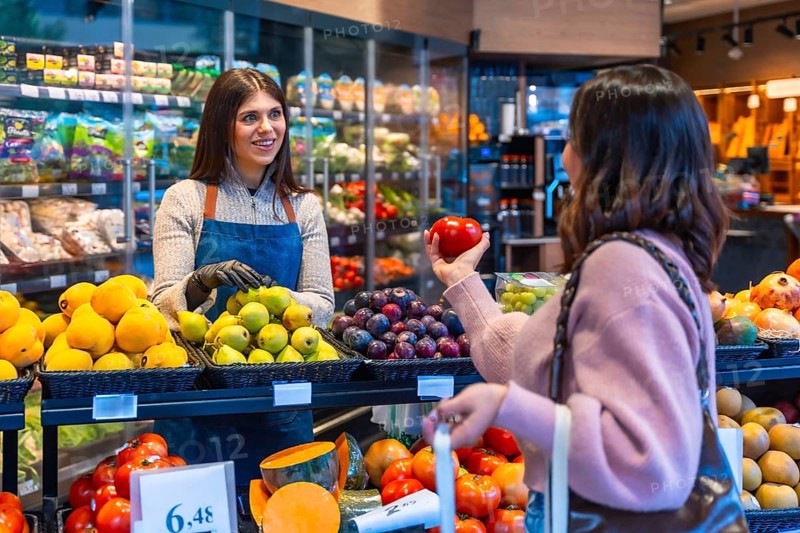 Friendly store employee warmly assisting a female customer selecting fresh organic produce at the healthy food section of a modern grocery store or supermarket