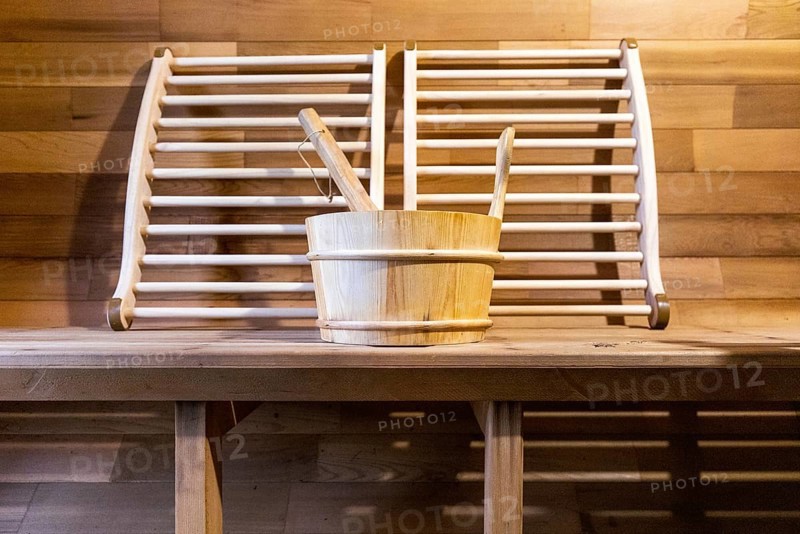 Steam and hot stone wooden cedar compact sauna interior with heating stone electrical device, hot water bucket and benches