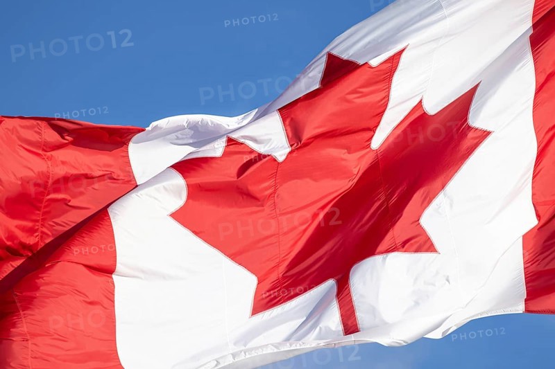 Red and white Canadian flag with a maple leaf waving in the air in downtown Toronto near Ontario Lake. Canadian patriotism and culture