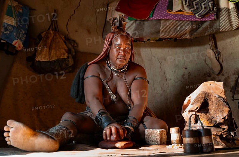 Elderly Himba woman making red paste for skin care, in a hut, traditional Himba village, Kaokoveld, Kunene, Namibia
