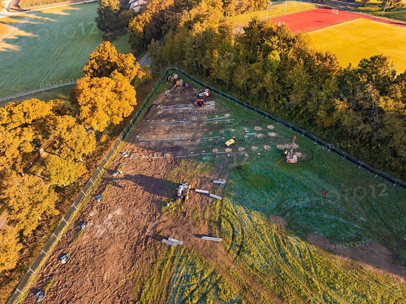 Construction site next to a sports field, surrounded by trees and shade, illuminated by morning light, PV FreifÃ¤chenanlage construction, Weil der Stadt, Germany
