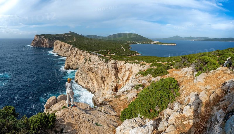 Tourist enjoying the view of steep cliffs by the sea, coastal landscape, cliffs on the Capo Caccia headland, Alghero, Sardinia, Italy